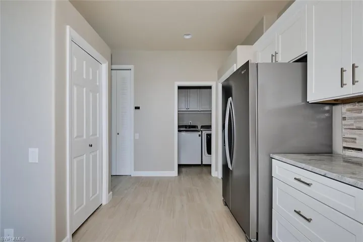 Kitchen featuring freestanding refrigerator, white cabinets, washer and dryer, and light stone counters