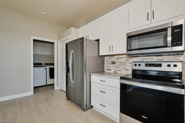 Kitchen featuring stainless steel appliances, white cabinetry, washing machine and dryer, decorative backsplash, and light stone countertops