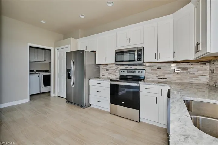 Kitchen with stainless steel appliances, white cabinetry, washer and clothes dryer, light stone countertops, and recessed lighting
