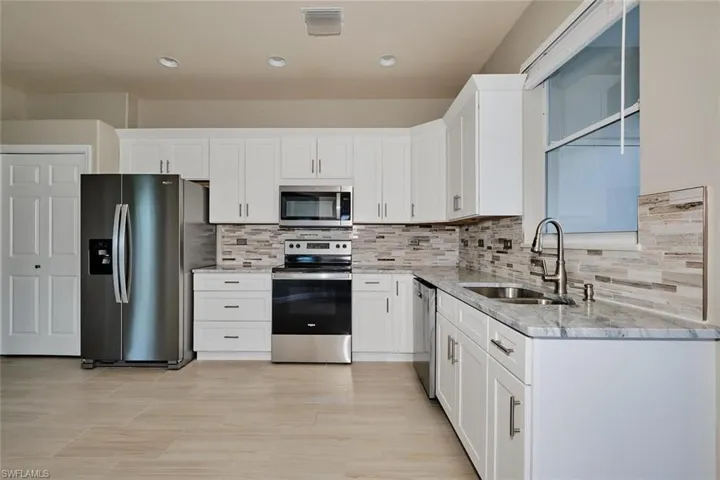 Kitchen with stainless steel appliances, white cabinets, light stone countertops, and recessed lighting