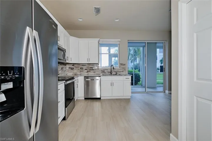 Kitchen featuring stainless steel appliances, white cabinetry, light stone countertops, backsplash, and recessed lighting