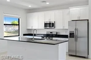 Kitchen with stainless steel appliances, white cabinets, a kitchen island with sink, dark countertops, and recessed lighting