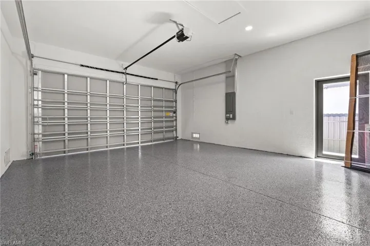 Spacious garage featuring a durable epoxy-coated floor, automatic overhead door opener, recessed lighting, and a frosted glass pedestrian door