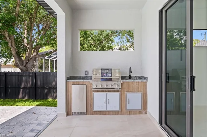 Outdoor kitchen featuring a built-in grill, integrated sink with a matte black faucet, and a stone-finish countertop
