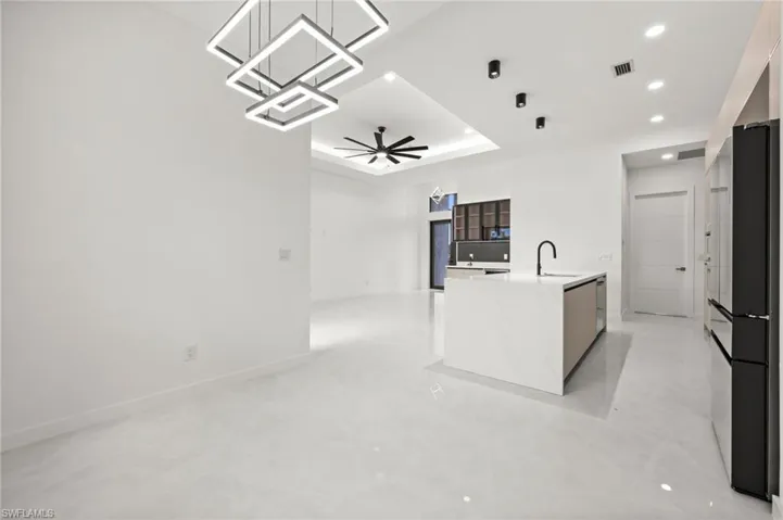 Open-concept living space featuring sleek tile flooring, a contemporary kitchen island with an integrated sink and matte black faucet, and modern square pendant lighting
