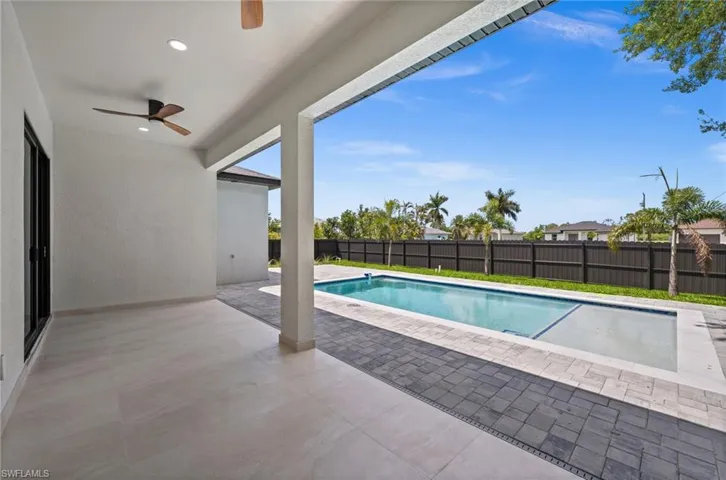 Expansive outdoor living area featuring a covered patio with recessed lighting and a ceiling fan, opening to a rectangular swimming pool with a sun shelf