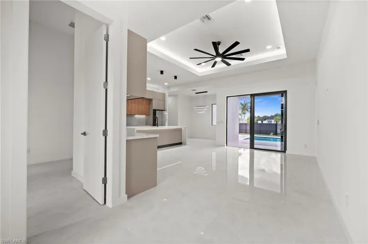 Spacious interior featuring large format tile flooring, a modern kitchen with two-tone cabinetry and an island, a tray ceiling with recessed lighting and a ceiling fan, and sliding glass doors opening to an outdoor area with a swimming pool