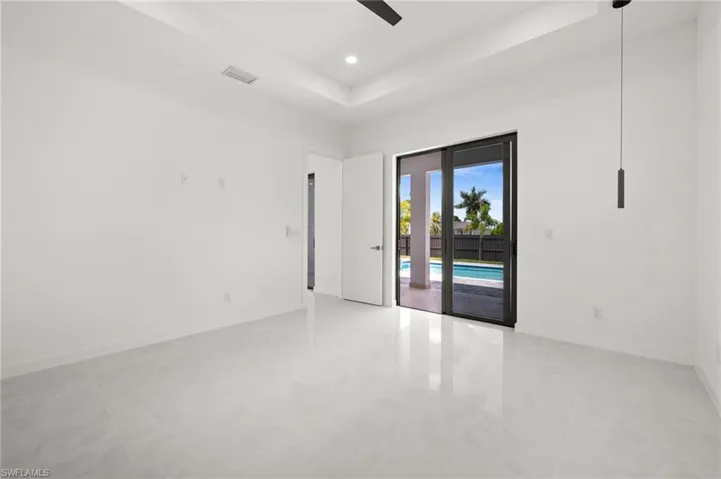 Spacious interior room featuring white walls, large format light-toned tile flooring, and a tray ceiling