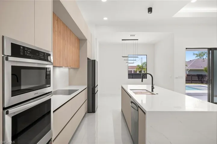 Contemporary kitchen featuring integrated stainless steel appliances, a built-in oven and microwave combination, and a large center island with an undermount sink and matte black faucet