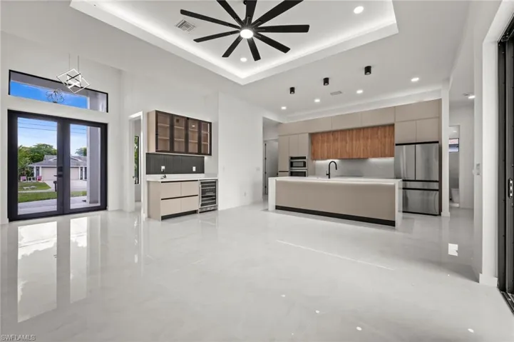 Open-concept living space with large format porcelain tile flooring and a tray ceiling featuring a ceiling fan and recessed lighting