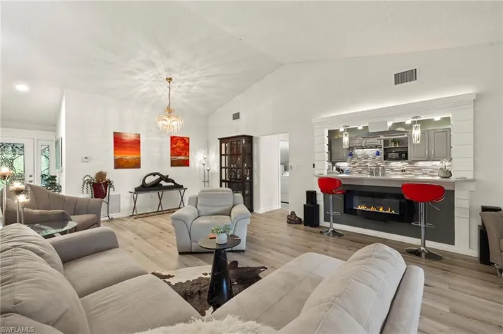 Living room featuring a glass covered fireplace, a chandelier, light wood-style floors, and vaulted ceiling