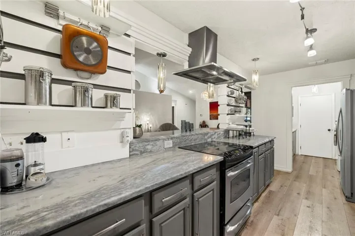 Kitchen with appliances with stainless steel finishes, island range hood, light stone counters, light wood-style floors, and gray cabinetry