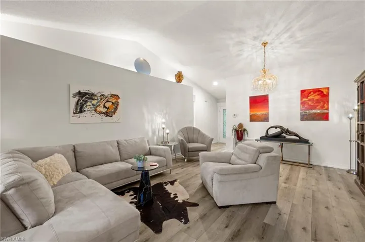 Living area with vaulted ceiling, light wood-style flooring, and a chandelier