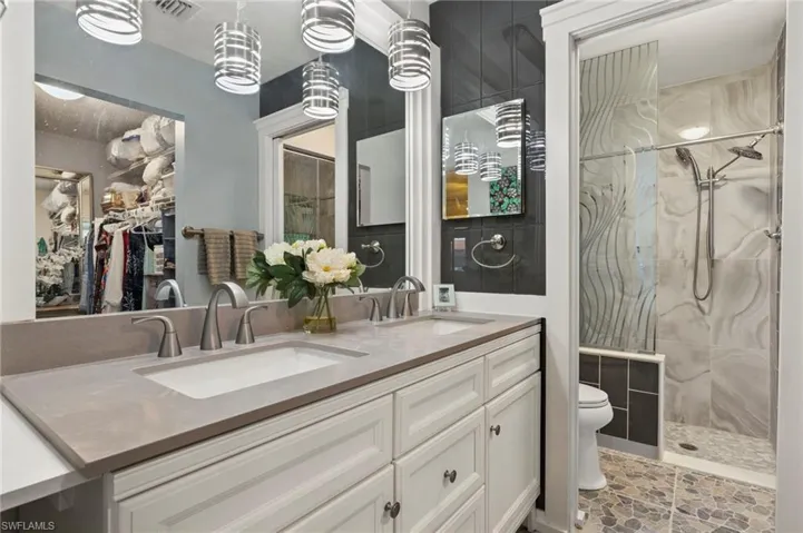 Full bath with double vanity, a shower stall, and a spacious closet