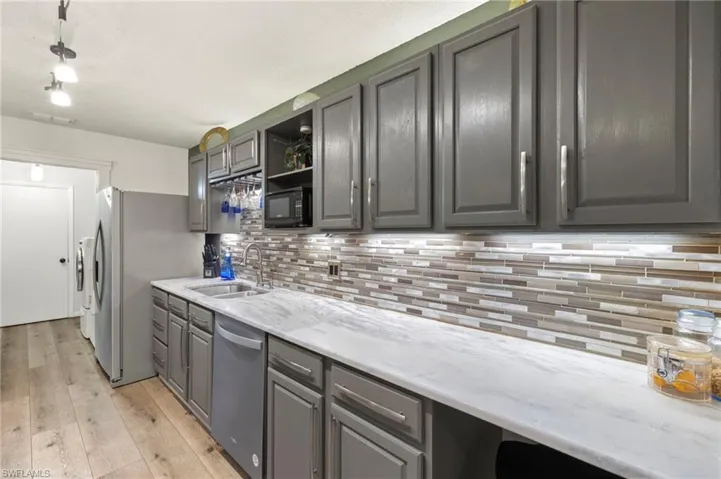 Kitchen with gray cabinetry, decorative backsplash, stainless steel appliances, and light stone countertops