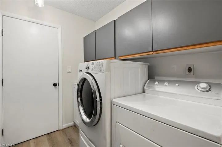 Laundry area featuring cabinet space, a textured ceiling, washing machine and dryer, and light wood-style flooring leads to the garage