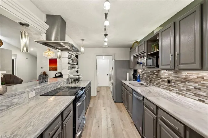 Kitchen featuring appliances with stainless steel finishes, island range hood, light wood-style floors, light stone countertops, and a textured ceiling