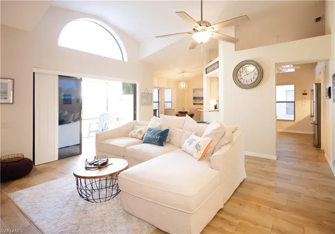 Living room with high vaulted ceiling, ceiling fan, light wood-type flooring, and a healthy amount of sunlight