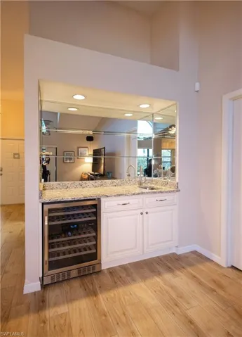 Bar featuring white cabinetry, light stone countertops, wine cooler, and light hardwood / wood-style flooring