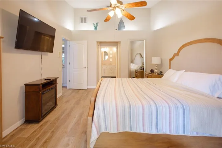 Bedroom featuring ceiling fan, a high ceiling, light hardwood / wood-style flooring, and ensuite bath