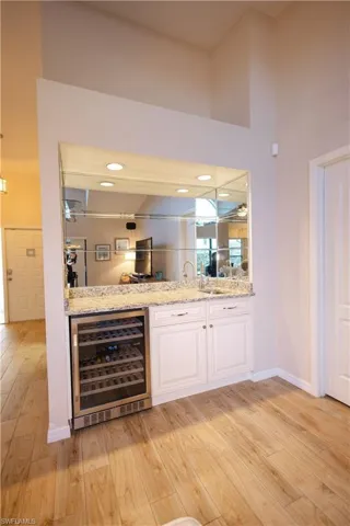 Bar with wine cooler, light hardwood / wood-style flooring, white cabinets, and light stone countertops
