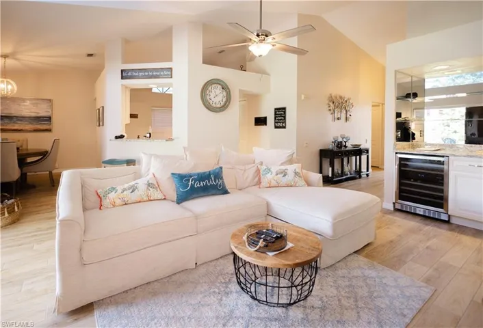 Living room with ceiling fan with notable chandelier, beverage cooler, and light wood-type flooring