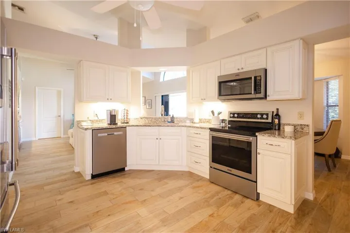 Kitchen with appliances with stainless steel finishes, light wood-type flooring, light stone counters, and ceiling fan