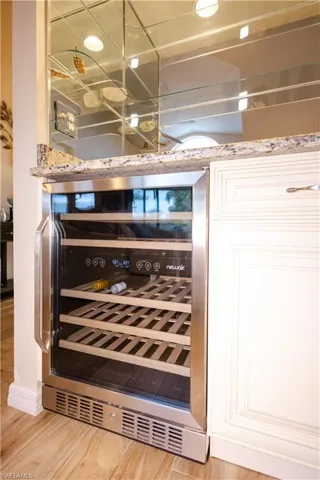 Details featuring light stone counters, light hardwood / wood-style floors, white cabinets, and wine cooler