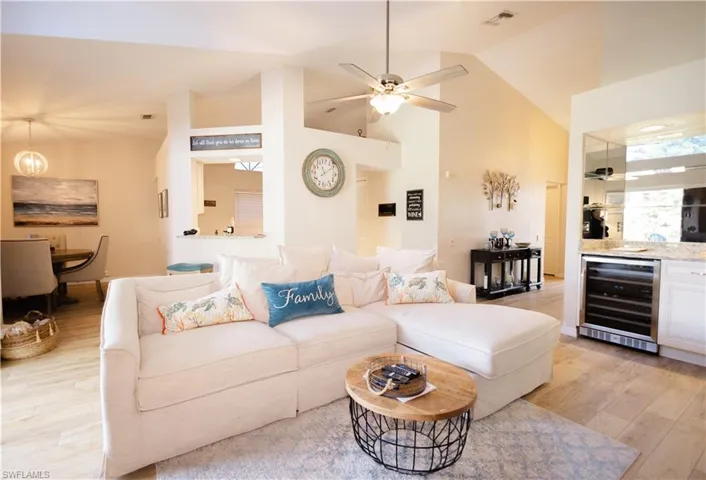 Living room with high vaulted ceiling, ceiling fan, beverage cooler, and light hardwood / wood-style flooring