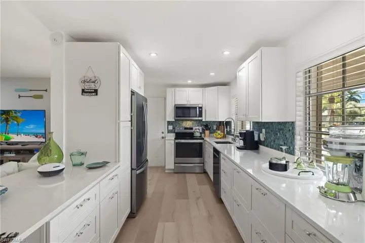 Kitchen with light wood-type flooring, sink, white cabinetry, appliances with stainless steel finishes, and light stone countertops