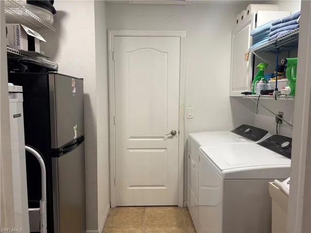 Laundry area featuring a textured wall, washer and dryer, and light tile patterned flooring