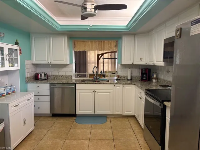 Kitchen with white cabinetry, stainless steel appliances, a tray ceiling, light stone countertops, and ceiling fan