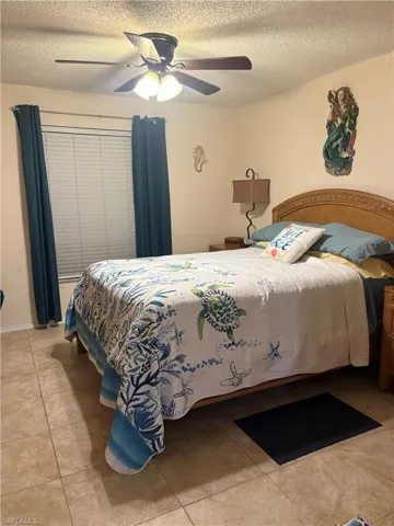 Bedroom with ceiling fan, a textured ceiling, and light tile patterned flooring