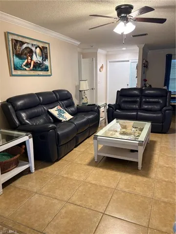 Living room featuring ornamental molding, a textured ceiling, light tile patterned floors, and ceiling fan