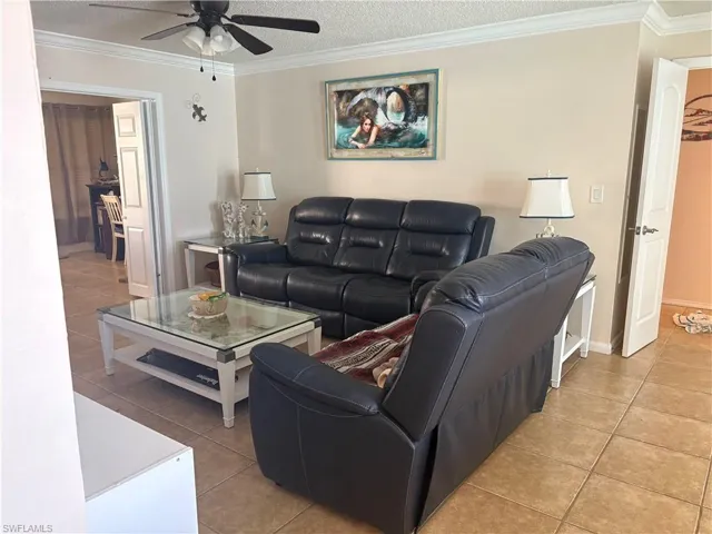 Living room featuring ornamental molding, light tile patterned floors, a textured ceiling, and ceiling fan