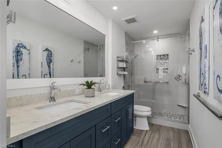 Bathroom with a shower stall, double vanity, recessed lighting, and wood finished floors
