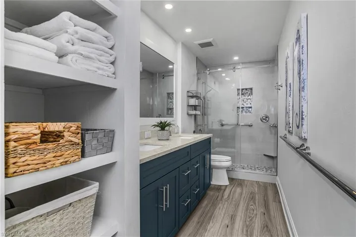 Full bathroom with a stall shower, double vanity, wood finished floors, and recessed lighting