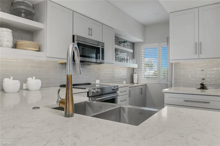 Kitchen featuring open shelves, appliances with stainless steel finishes, light stone counters, and decorative backsplash