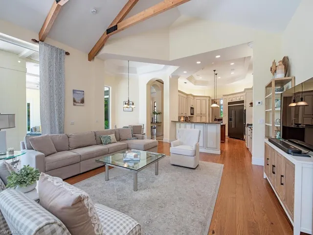 Living room with light wood-type flooring, arched walkways, a tray ceiling, recessed lighting, and high vaulted ceiling