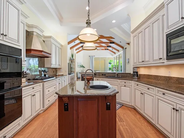 Kitchen with dark stone counters, black appliances, light wood-style flooring, pendant lighting, and a peninsula