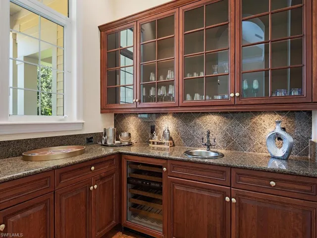 Bar featuring beverage cooler, decorative backsplash, dark stone counters, and glass insert cabinets