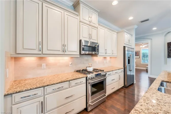 Kitchen featuring appliances with stainless steel finishes, crown molding, dark wood-type flooring, decorative backsplash, and recessed lighting