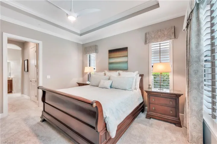 Bedroom with light colored carpet, ornamental molding, a raised ceiling, and baseboards