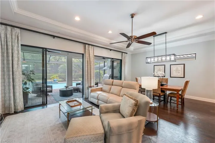 Living room featuring a raised ceiling, ornamental molding, a ceiling fan, wood finished floors, and recessed lighting