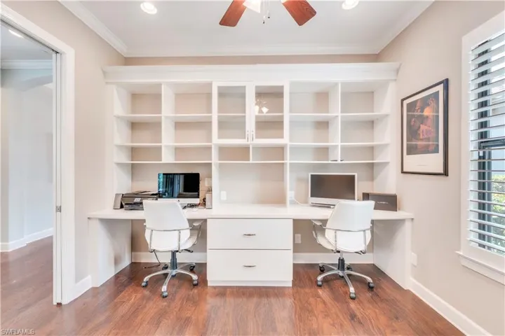 Unfurnished office with built in desk, wood finished floors, a ceiling fan, ornamental molding, and baseboards