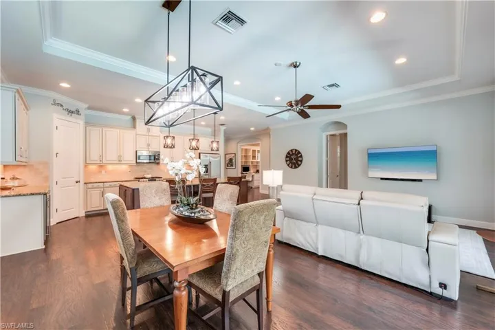 Dining space with a raised ceiling, crown molding, arched walkways, dark wood-style floors, and recessed lighting
