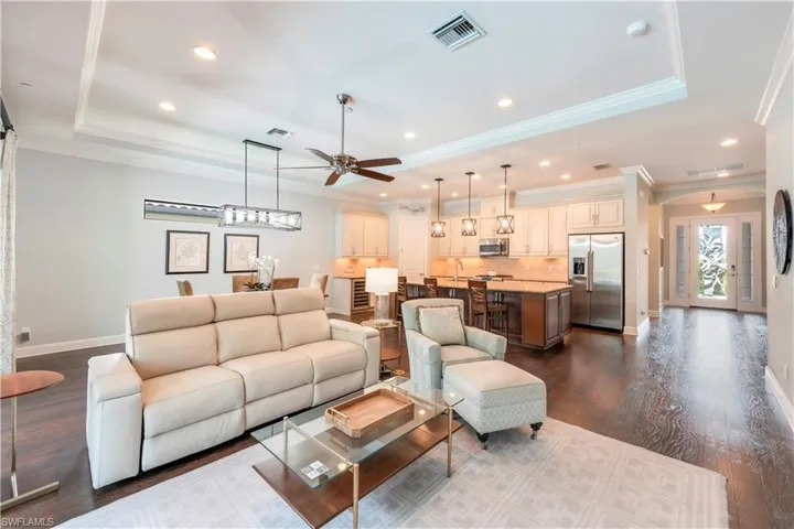 Living area with a raised ceiling, crown molding, a ceiling fan, baseboards, and dark wood-style floors