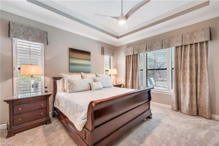 Bedroom with light colored carpet, ornamental molding, baseboards, a tray ceiling, and a ceiling fan