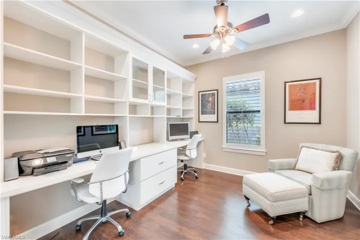 Office area with crown molding, dark wood finished floors, baseboards, ceiling fan, and built in desk
