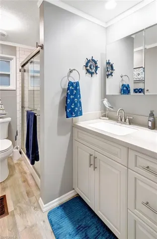 Bathroom featuring hardwood / wood-style floors, toilet, a shower with door, vanity, and ornamental molding